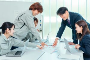 資料とパソコンを使って打ち合わせをする、作業着とスーツ姿の担当者たち
